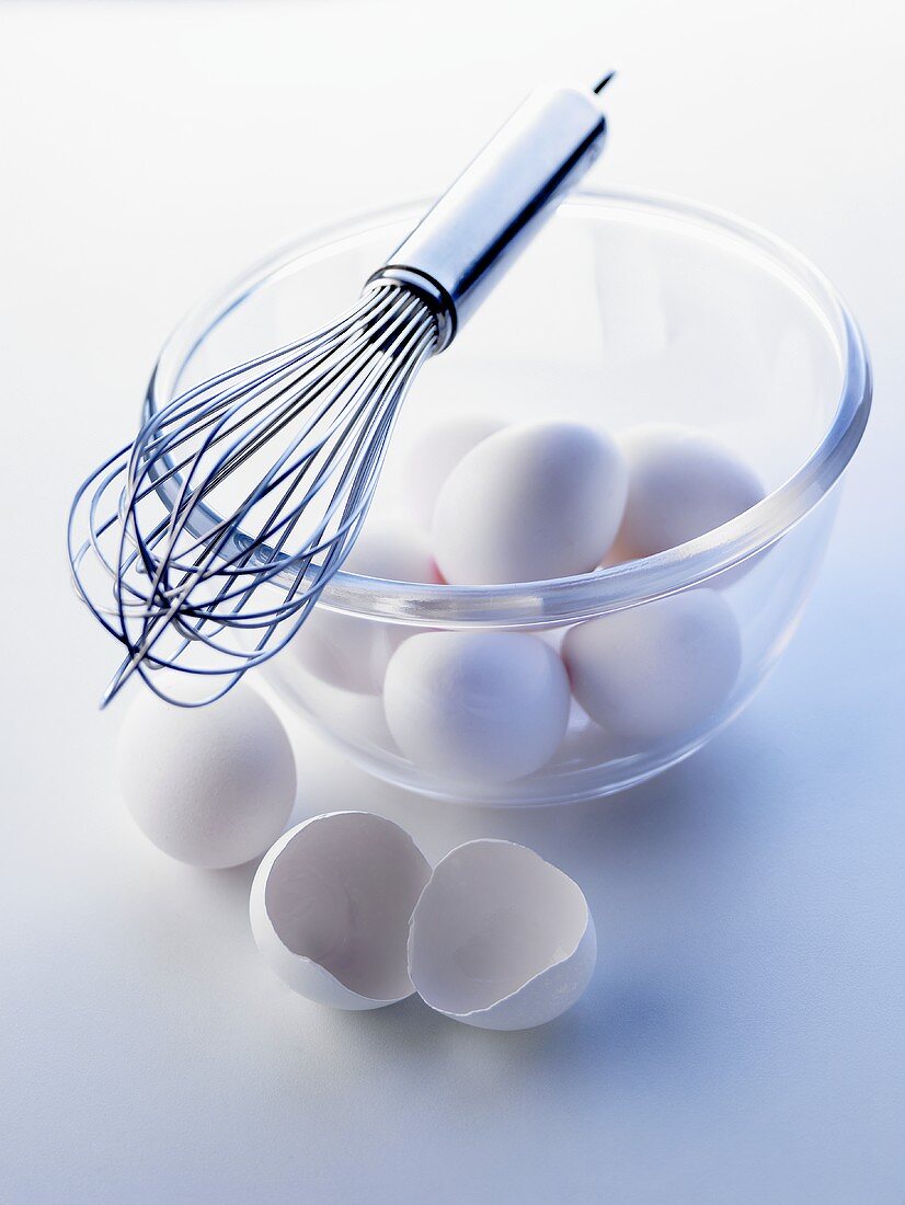 weiße Eier in einer Glasschüssel, Schneebesen obenauf