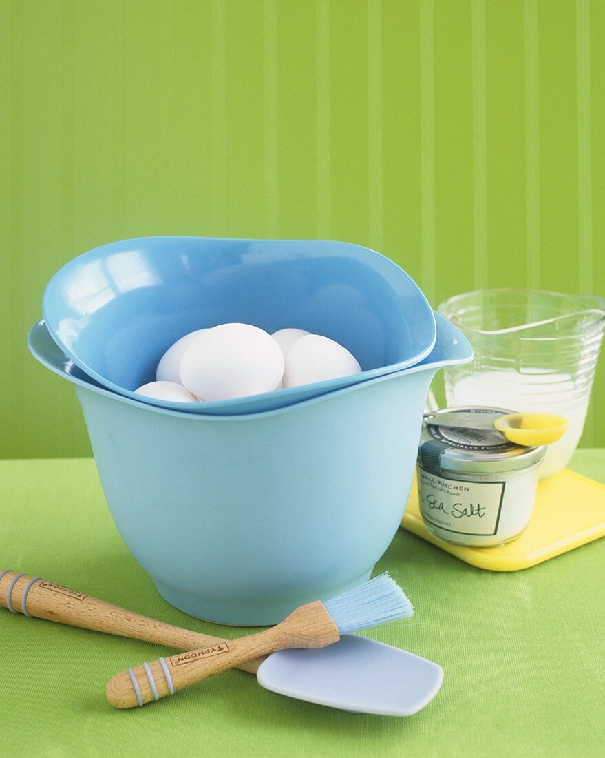Fresh eggs in mixing bowl surrounded by baking utensils