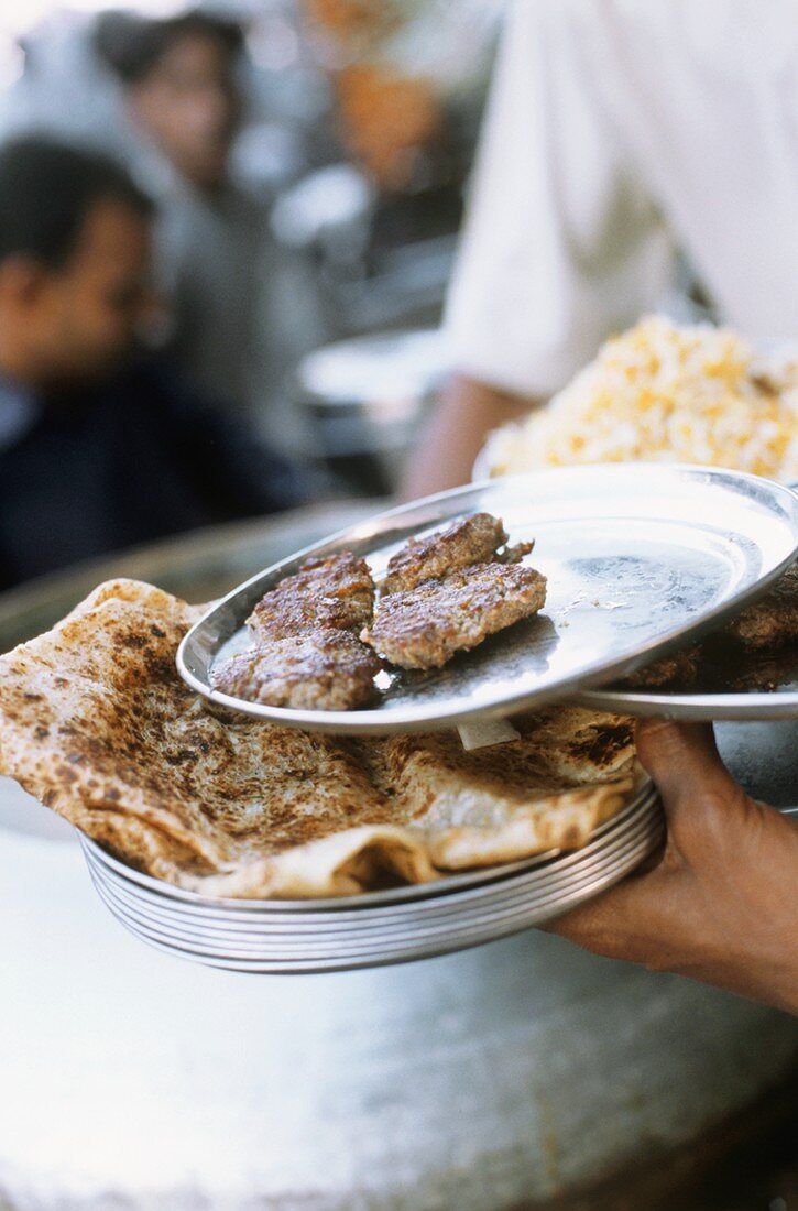 Mann serviert Lammfrikadellen & indisches Brot im Restaurant