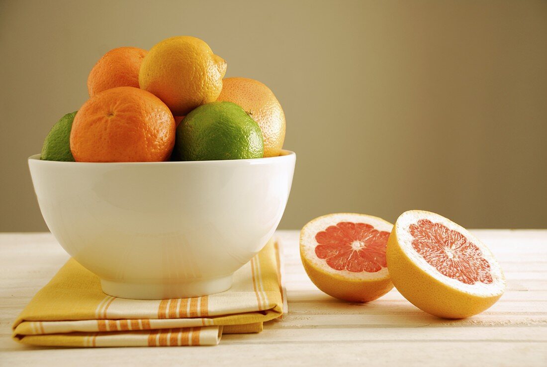 Citrus fruits in a bowl, halved grapefruit beside it
