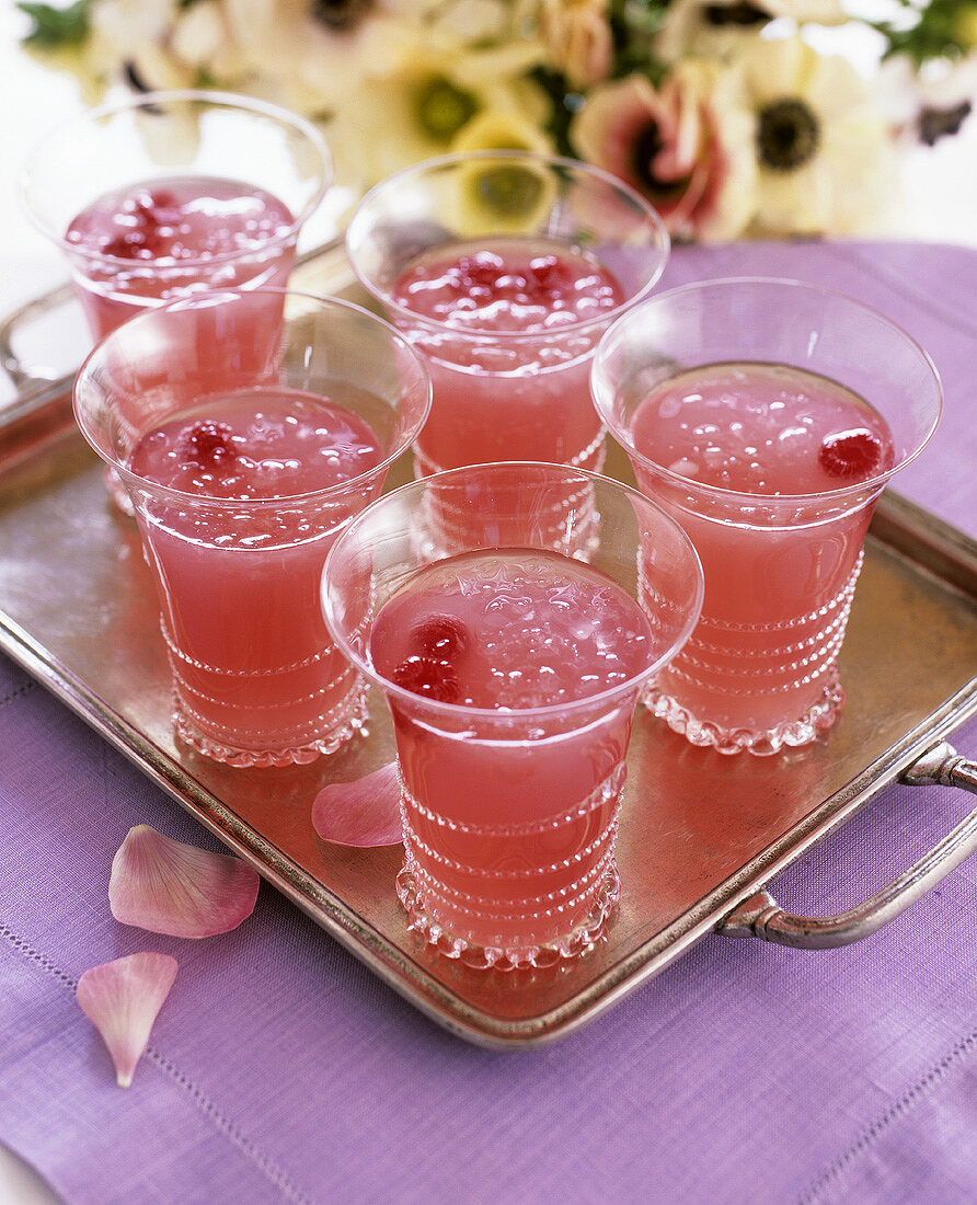 Pink drink with raspberries, ice cubes and rose petals