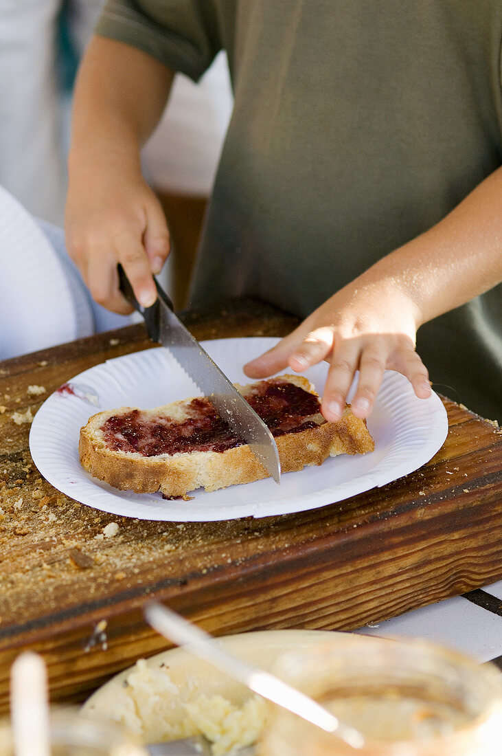 Kinderhände zerschneiden ein Marmeladenbrot mit einem Messer