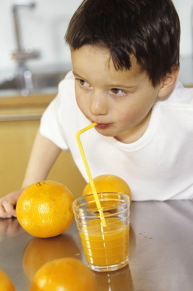 Kleiner Junge trinkt Orangensaft mit Strohhalm