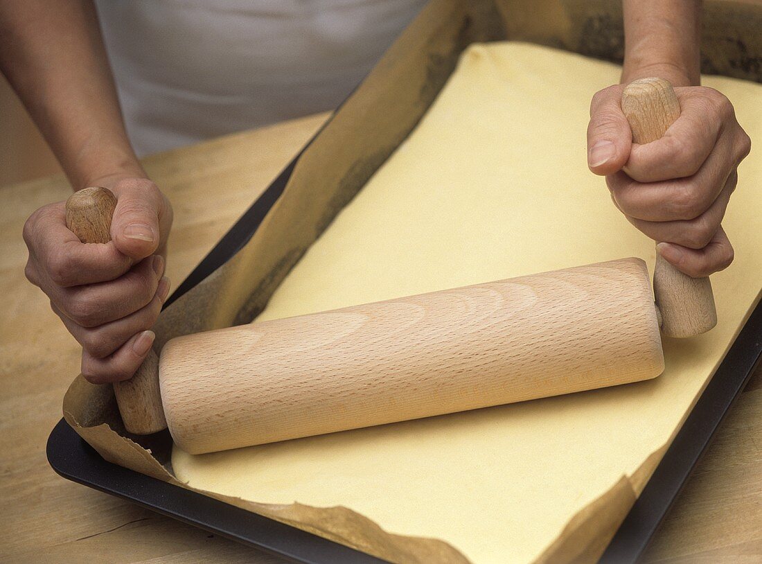 Rolling pin with folding handles on yeast dough in baking tray