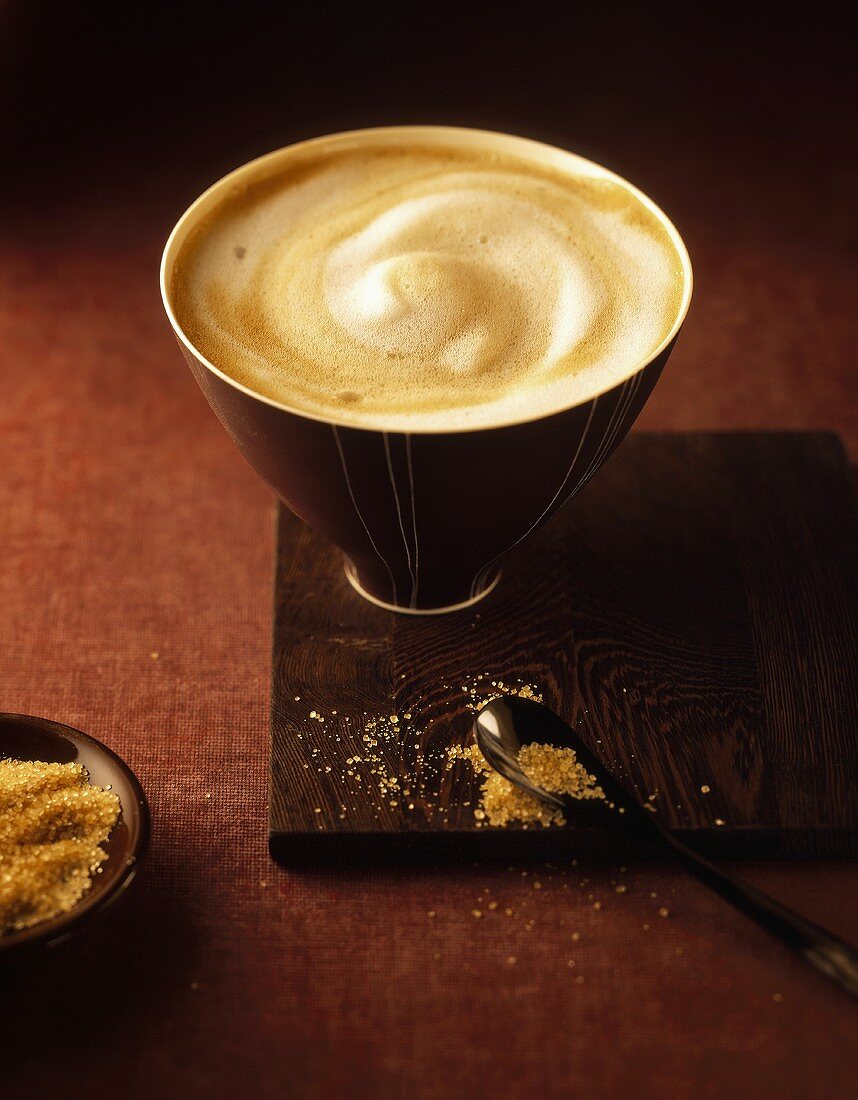 Milchkaffee in einer Schale, davor brauner Zucker