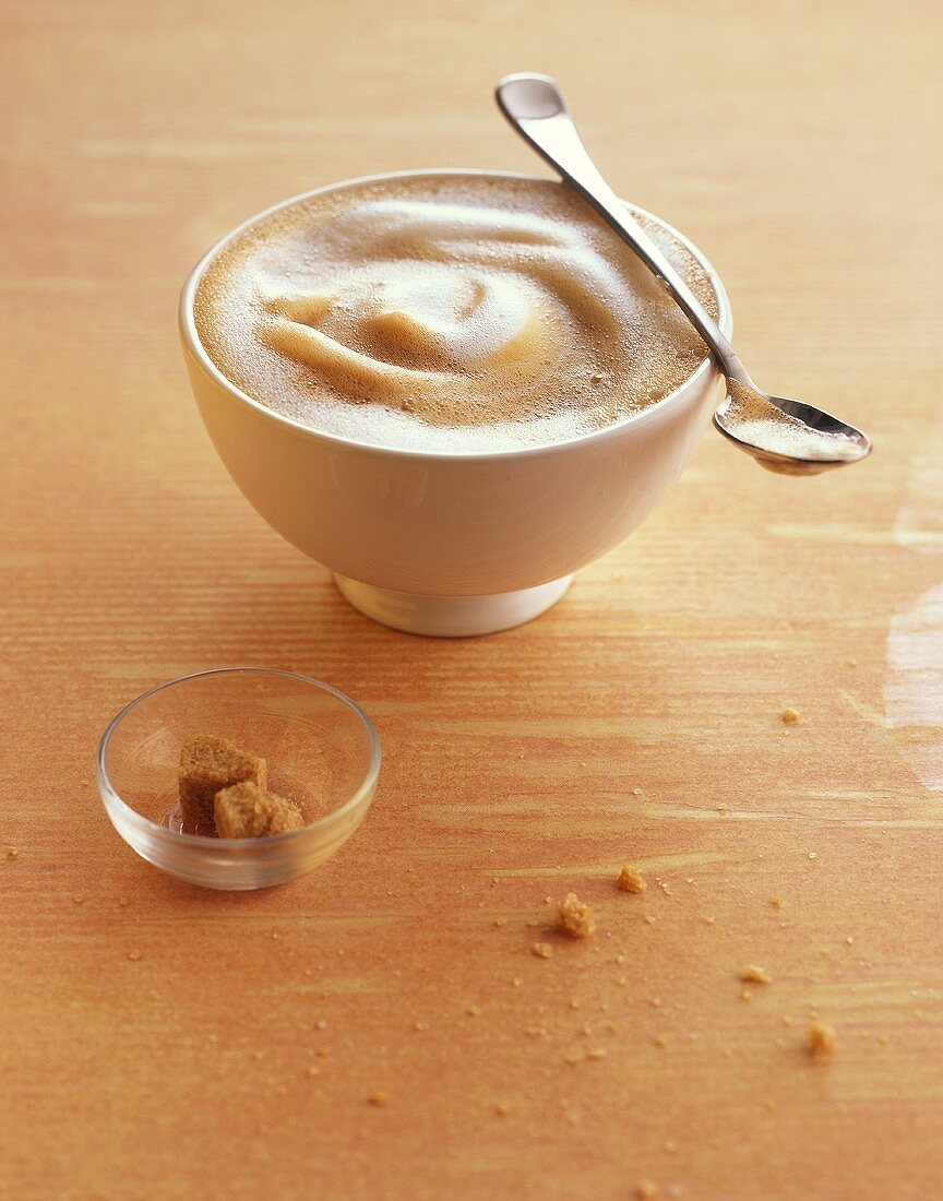 Milky coffee in a bowl, spoon and sugar cubes