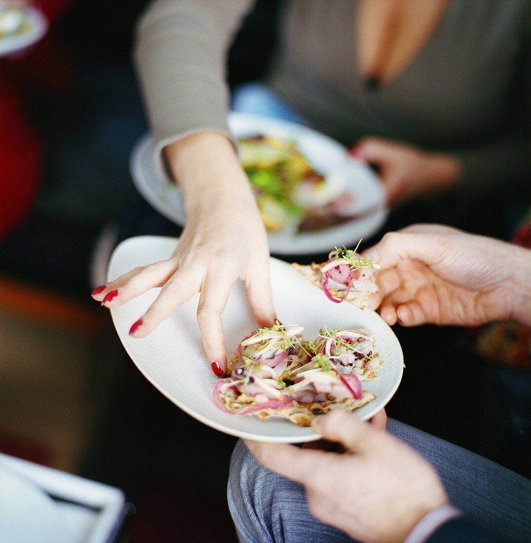 Woman reaching for appetiser (herring terrine on flatbread triangle)