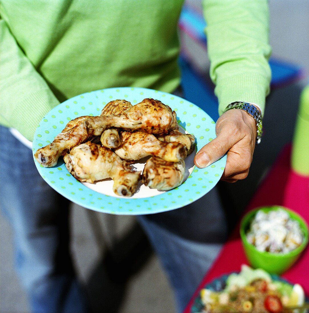 Man holding plate of grilled chicken legs