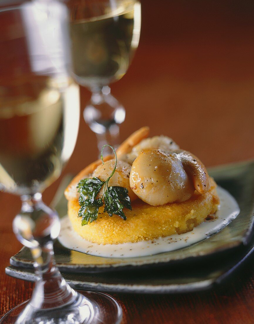Polenta cake topped with scallops, two glasses of white wine