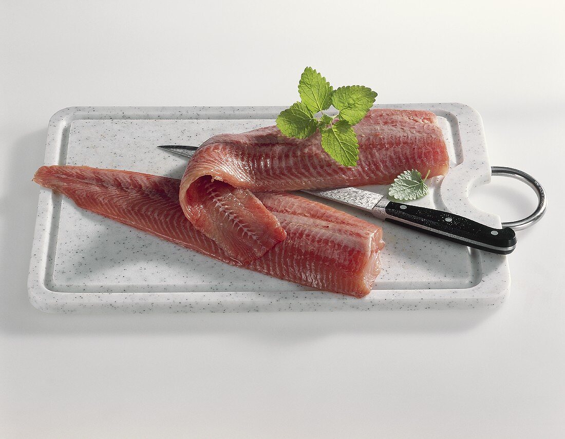 Two catfish fillets with knife on a board