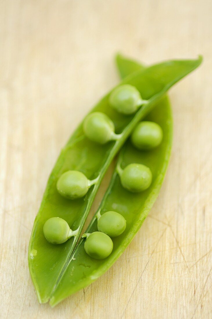 An opened pea pod on a wooden background