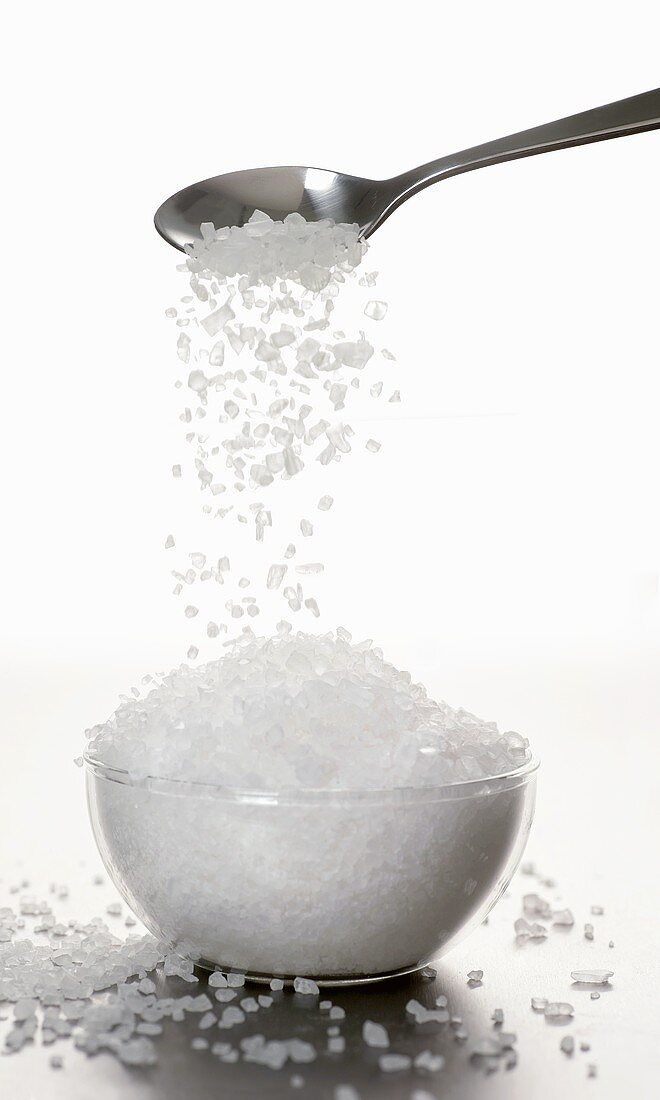 Sea salt trickling from spoon into a small bowl