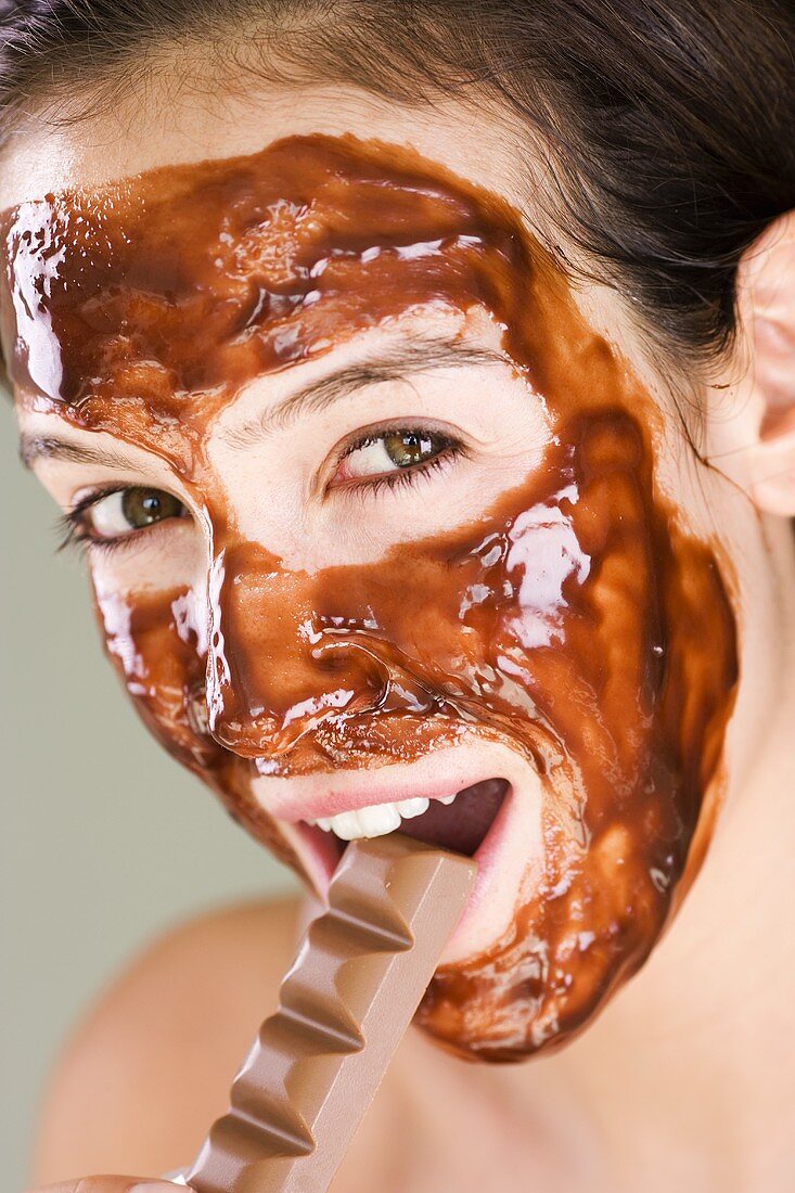 Frau mit Schokoladen-Maske isst Schokoladenriegel