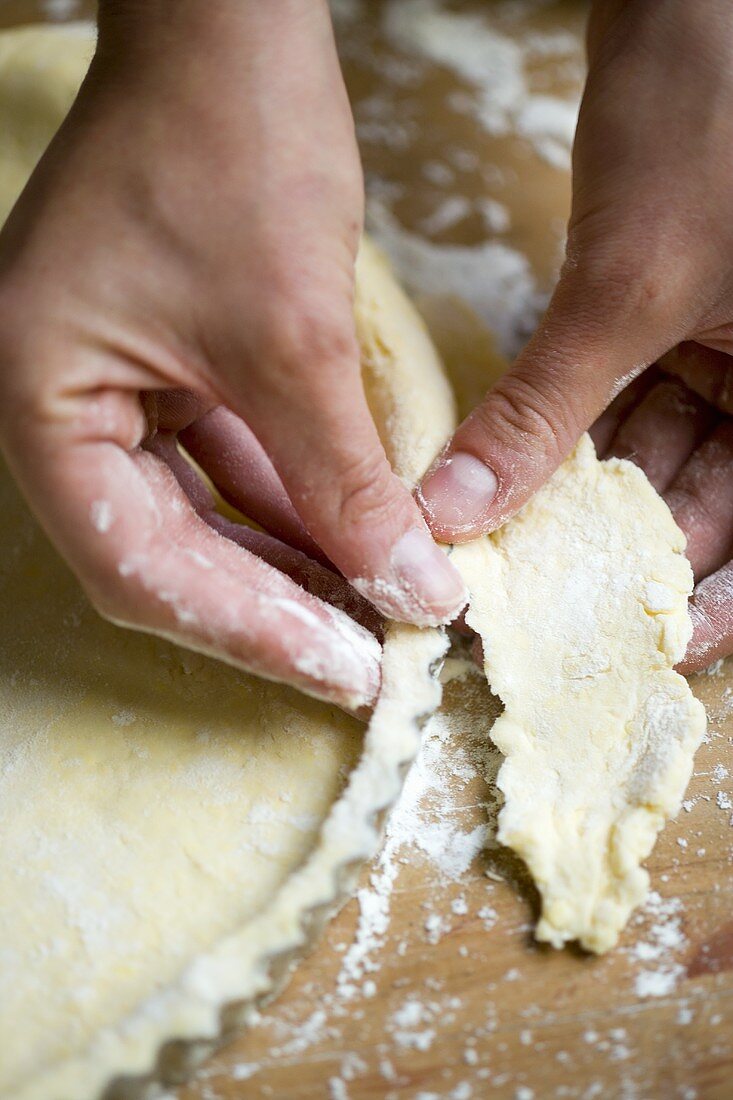 Hands pressing pastry onto the sides of a tart tin