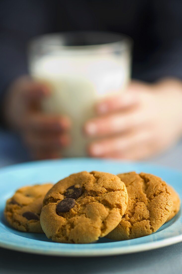 Kekse mit Schokoflocken, im Hintergrund Kind mit Milchglas