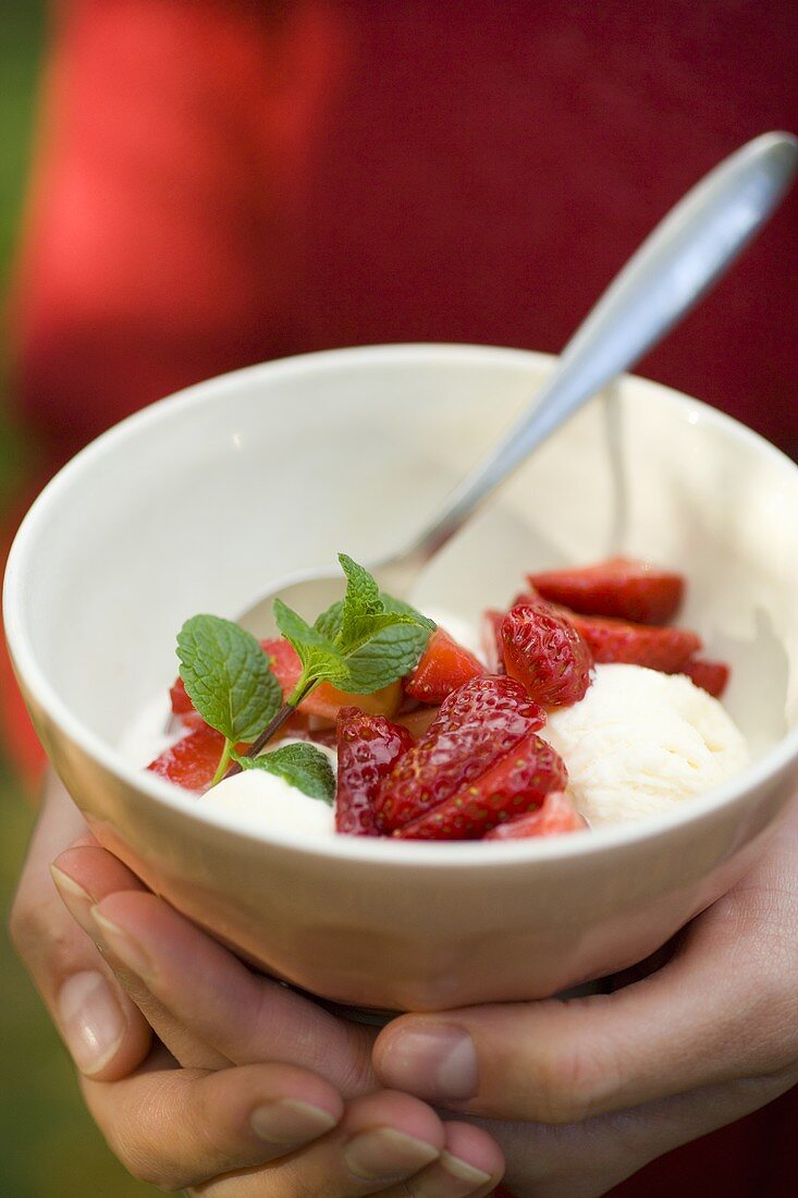 Zwei Hände halten ein Schälchen mit Vanilleeis und Erdbeeren