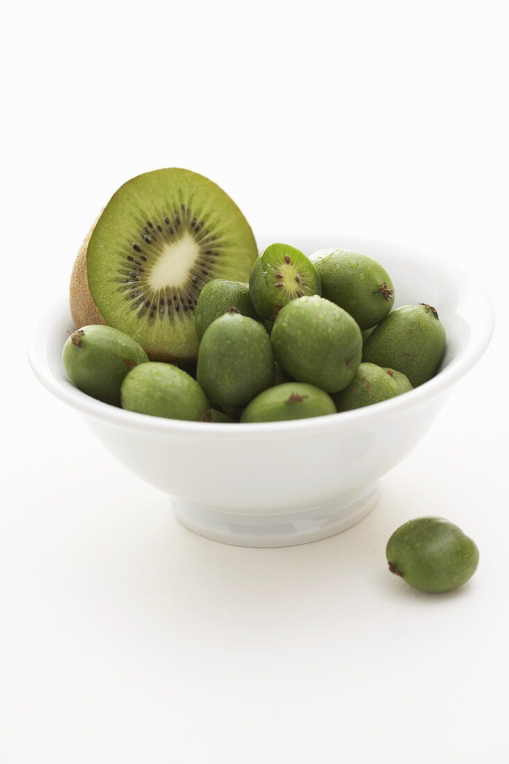 Half a kiwi fruit and baby kiwi fruits in a small bowl
