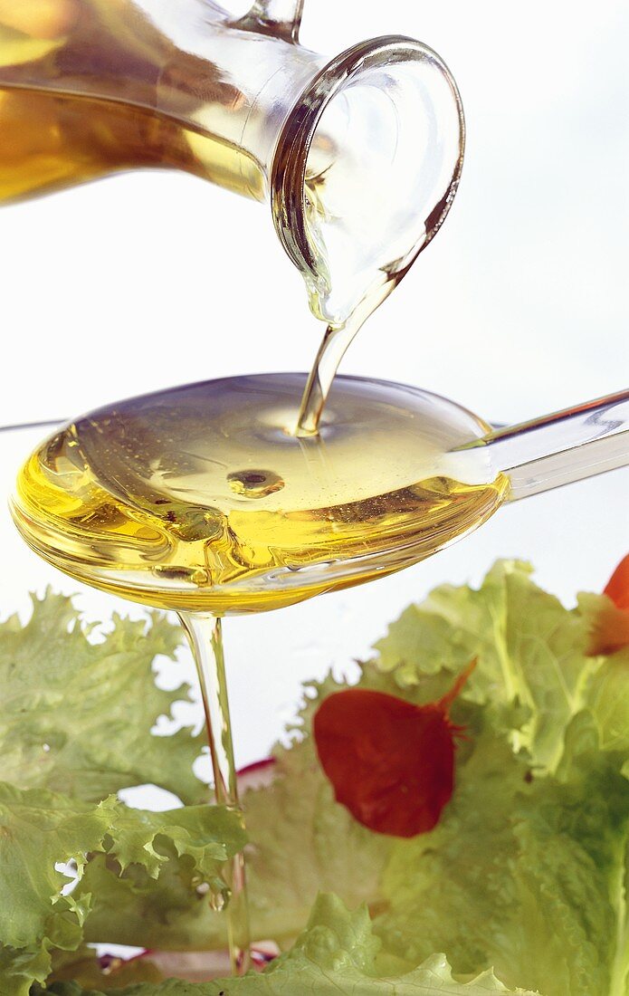 Olive oil running over spoon onto salad