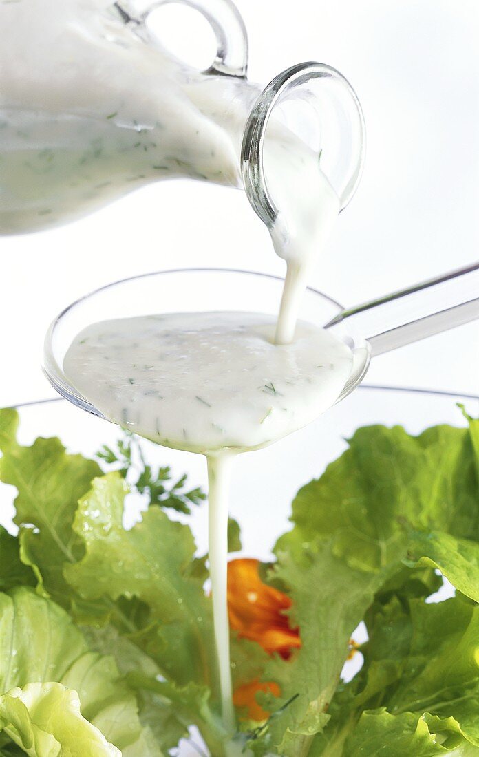 Joghurt-Vinaigrette über Löffel auf Salat fliessend