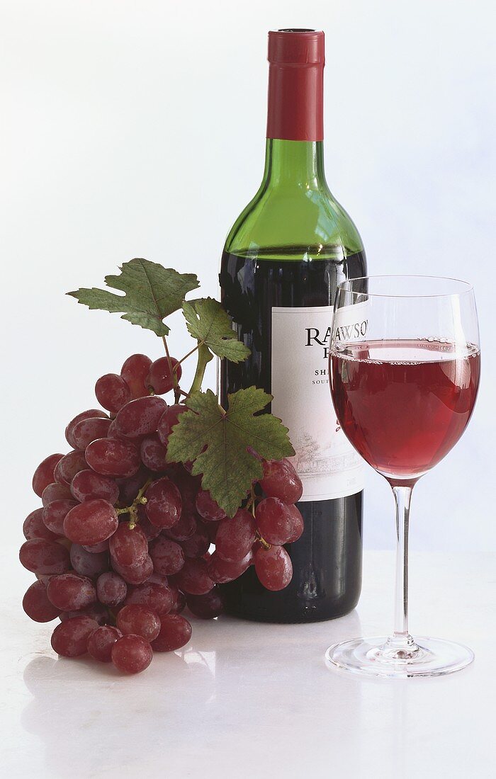 Eine Flasche Rotwein mit Rotweinglas und Trauben