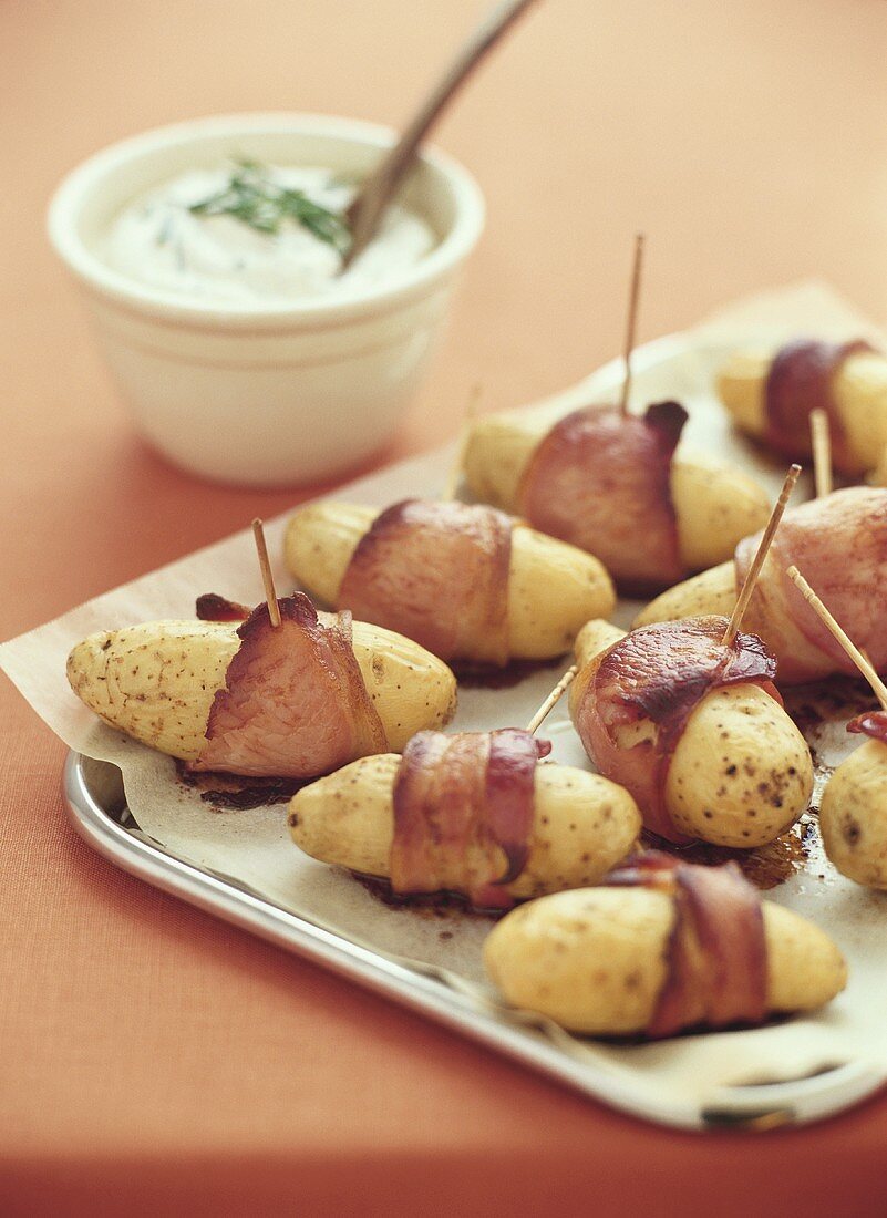 Baked potatoes wrapped in bacon with sour cream dip