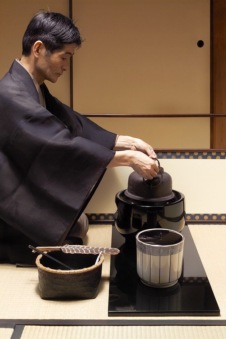 Tea master at tea ceremony, putting kettle on