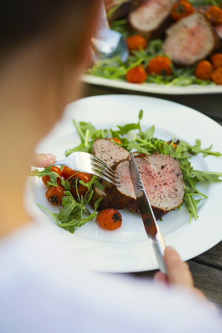 Model eating roast beef with roasted tomatoes and rocket