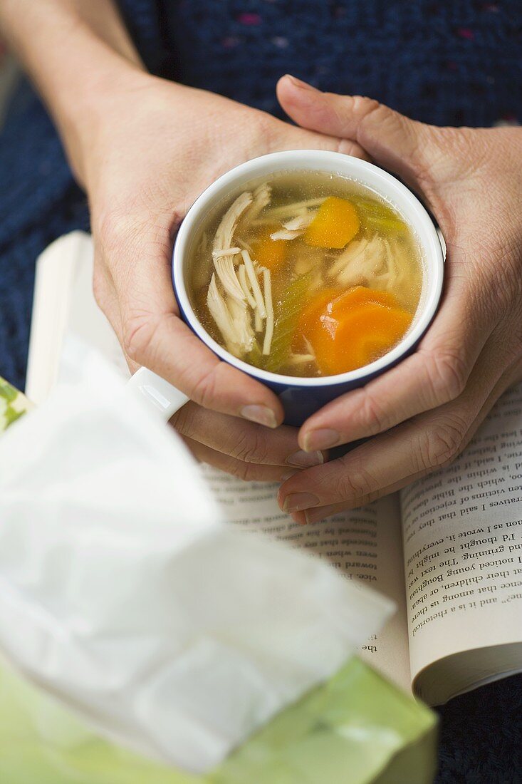 Hände halten eine Tasse Hähnchen-Nudel-Suppe mit Gemüse