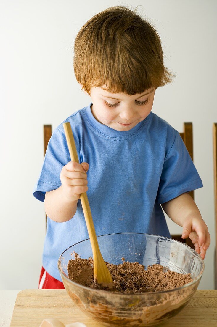 Small boy stirring cake mixture with a wooden spoon
