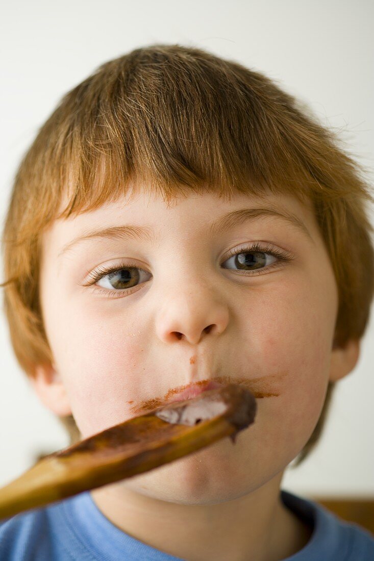 Small boy licking a wooden spoon