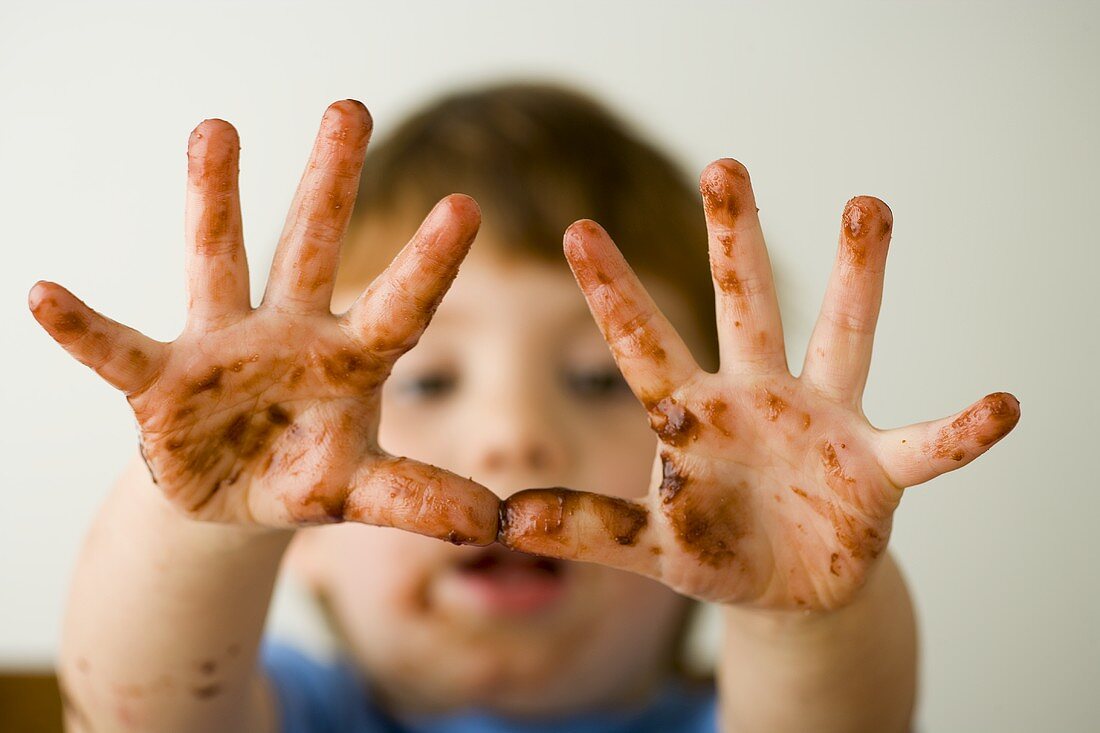 Kleiner Junge mit Schokoladen-Händen