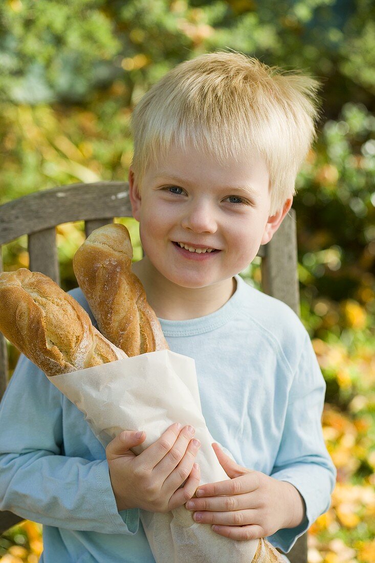 Blond boy holding two baguette sticks in paper