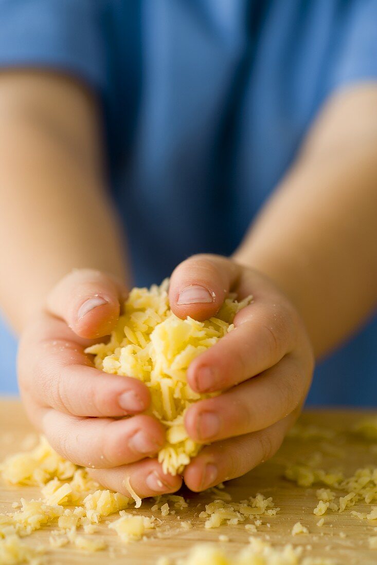 Child's hands holding grated cheese
