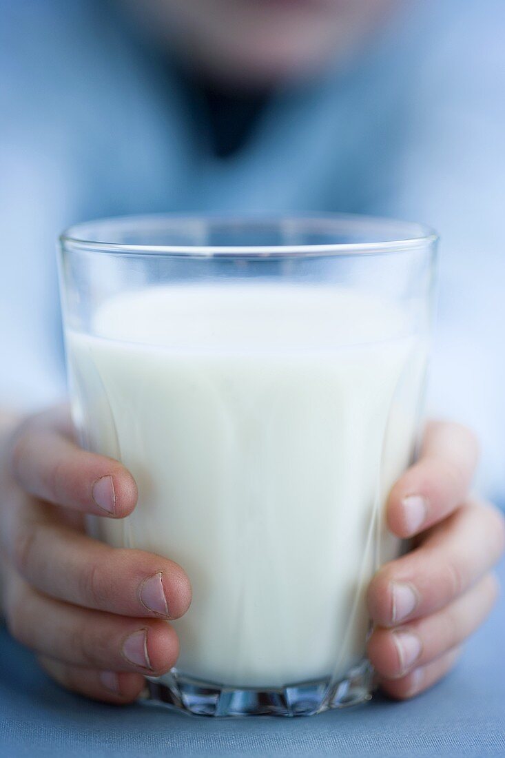 Child's hands holding a glass of milk
