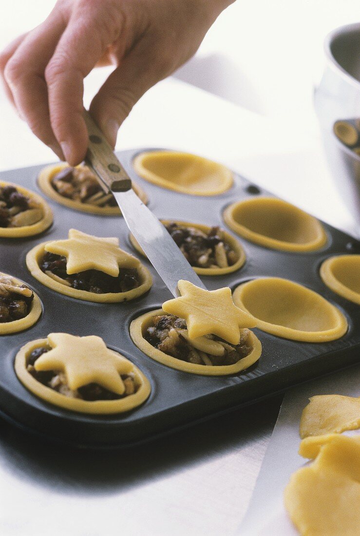 Putting pastry stars on top of mincemeat tarts