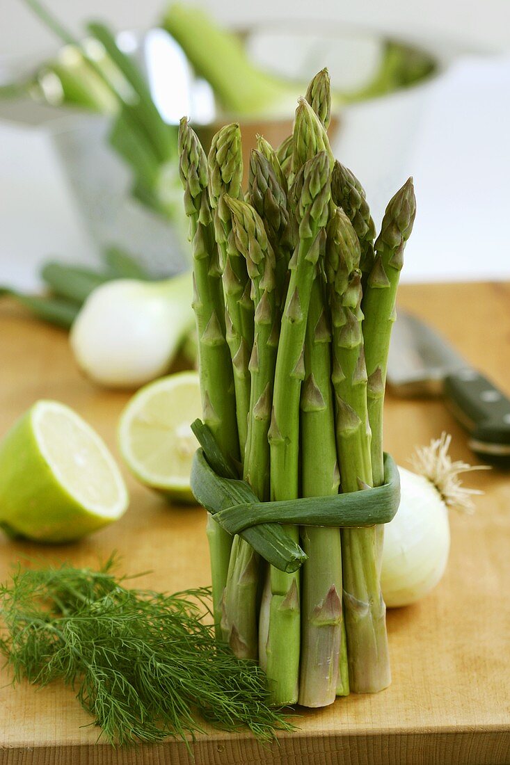 Bundle of asparagus on wooden board, vegetables in background