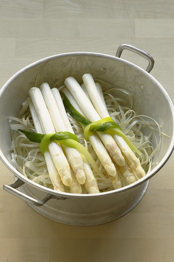 Two bundles of asparagus on asparagus peelings in colander