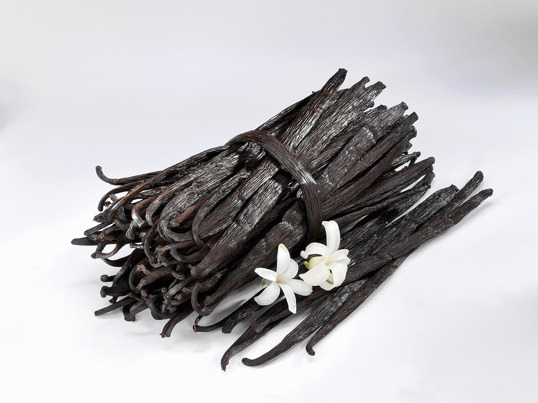 A bundle of vanilla pods and loose pods with two flowers