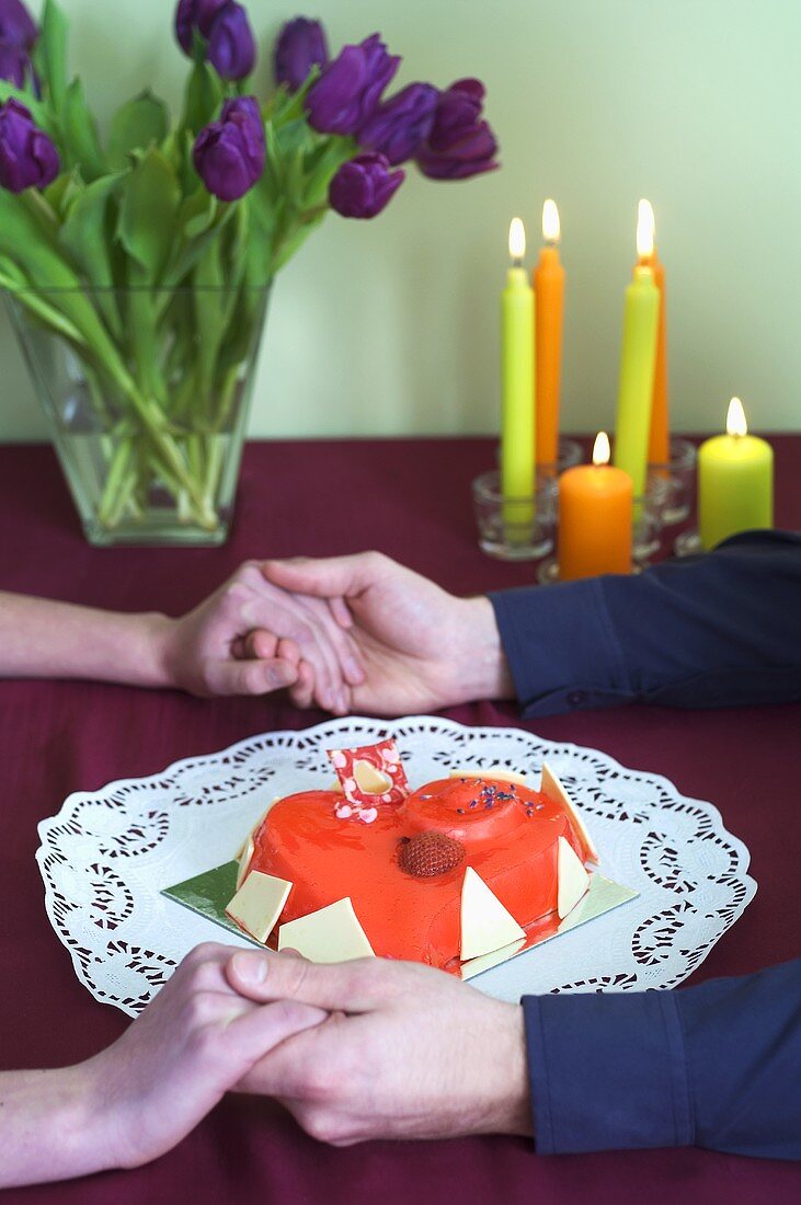 Couple's hands around heart-shaped cake