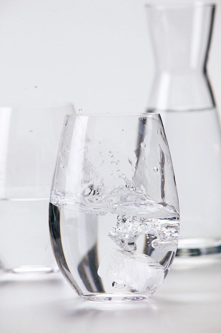 Ein Eiswüfel fällt in ein Glas Mineralwasser