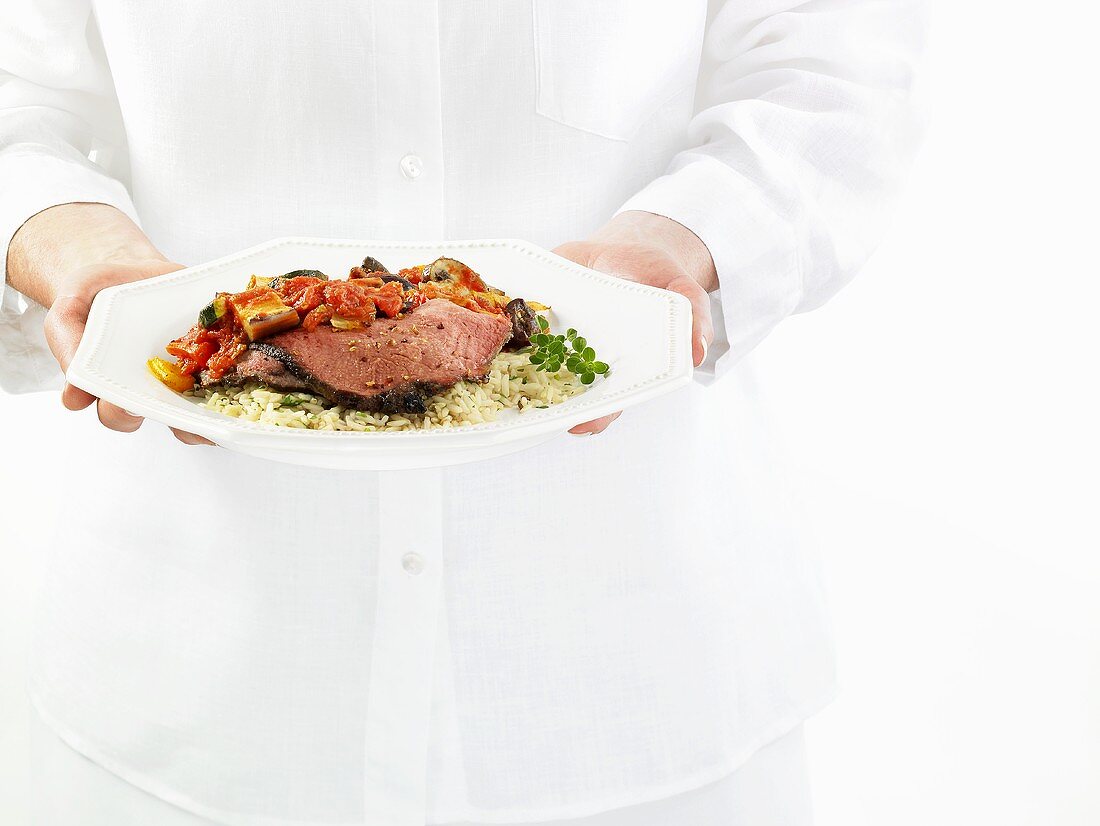 Hands holding beef with ratatouille and rice