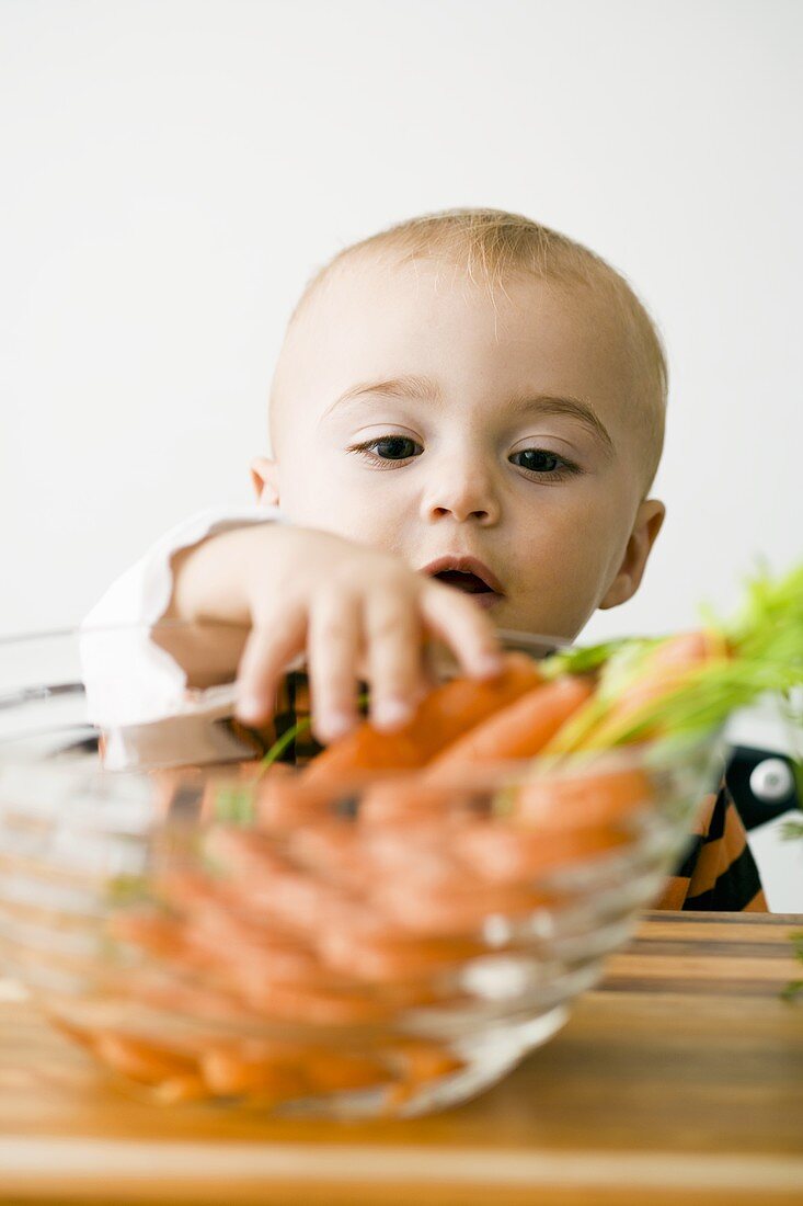 Small boy reaching into bowl of carrots