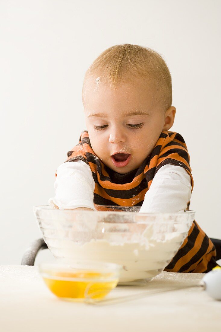 Small boy with both hands in bowl of flour