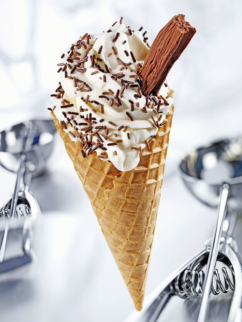 Cone of soft vanilla ice cream, chocolate sprinkles & flake