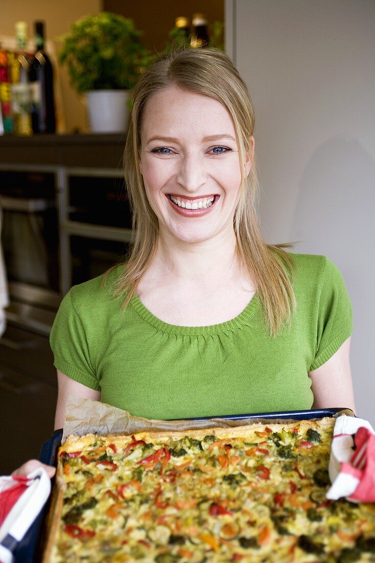 Junge Frau hält Blech mit Gemüsepizza in den Händen