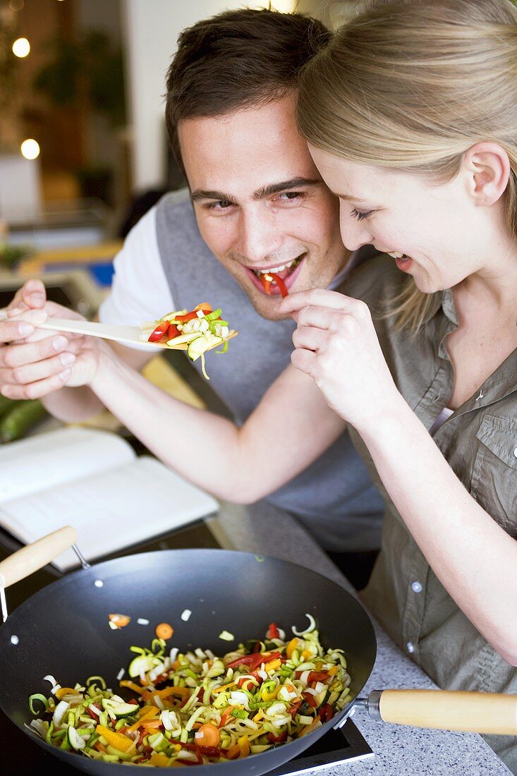Young couple tasting vegetables cooked in wok