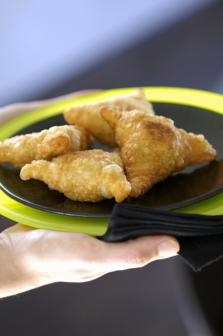 Hand holding plate of samosas