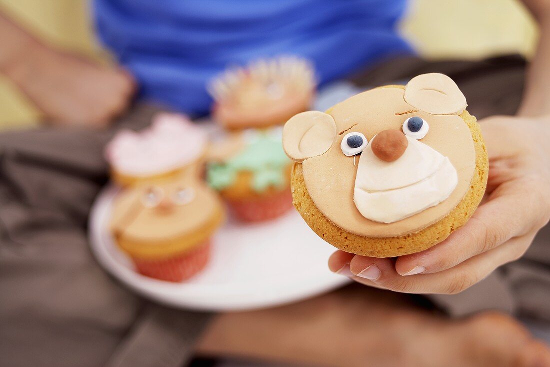 Hand hält Muffin mit Bären-Gesicht