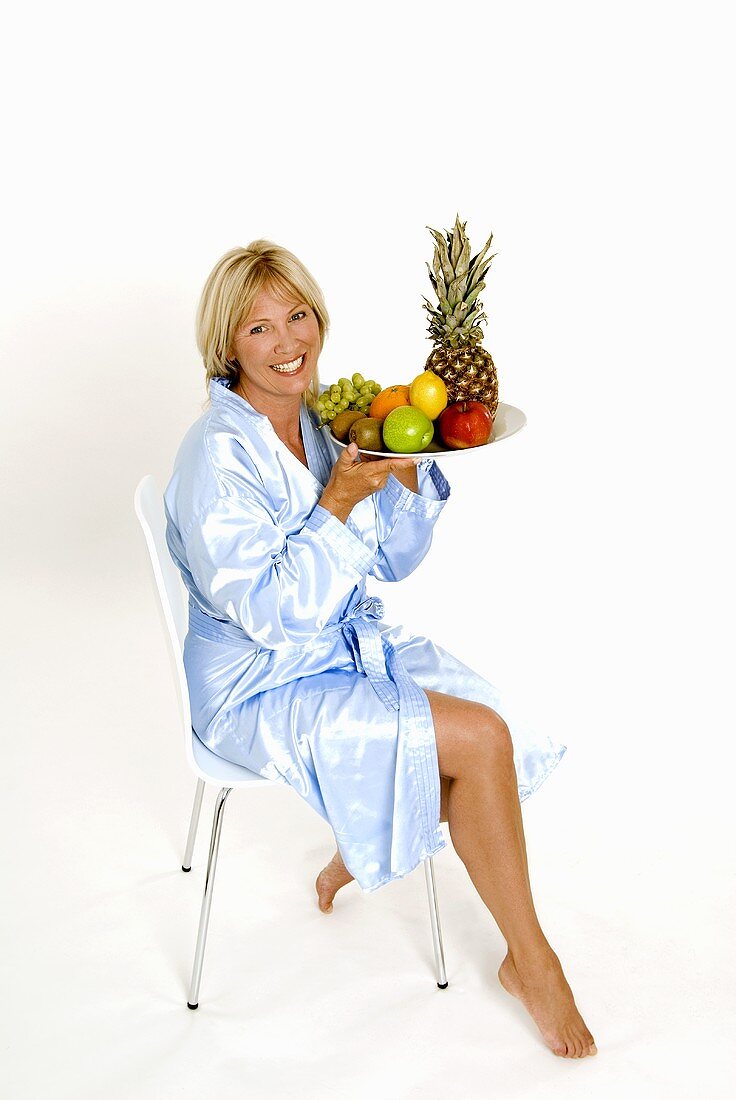 Frau sitzt auf einem Stuhl mit Obstschale in der Hand
