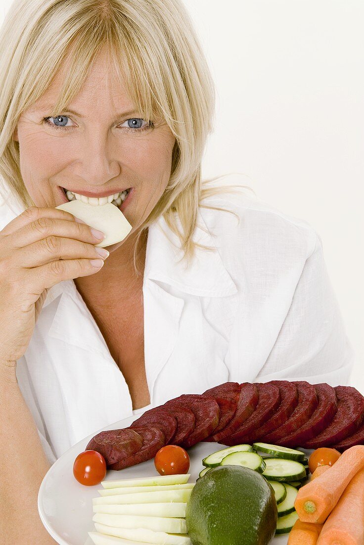 Woman with plate of vegetables biting into slice of kohlrabi